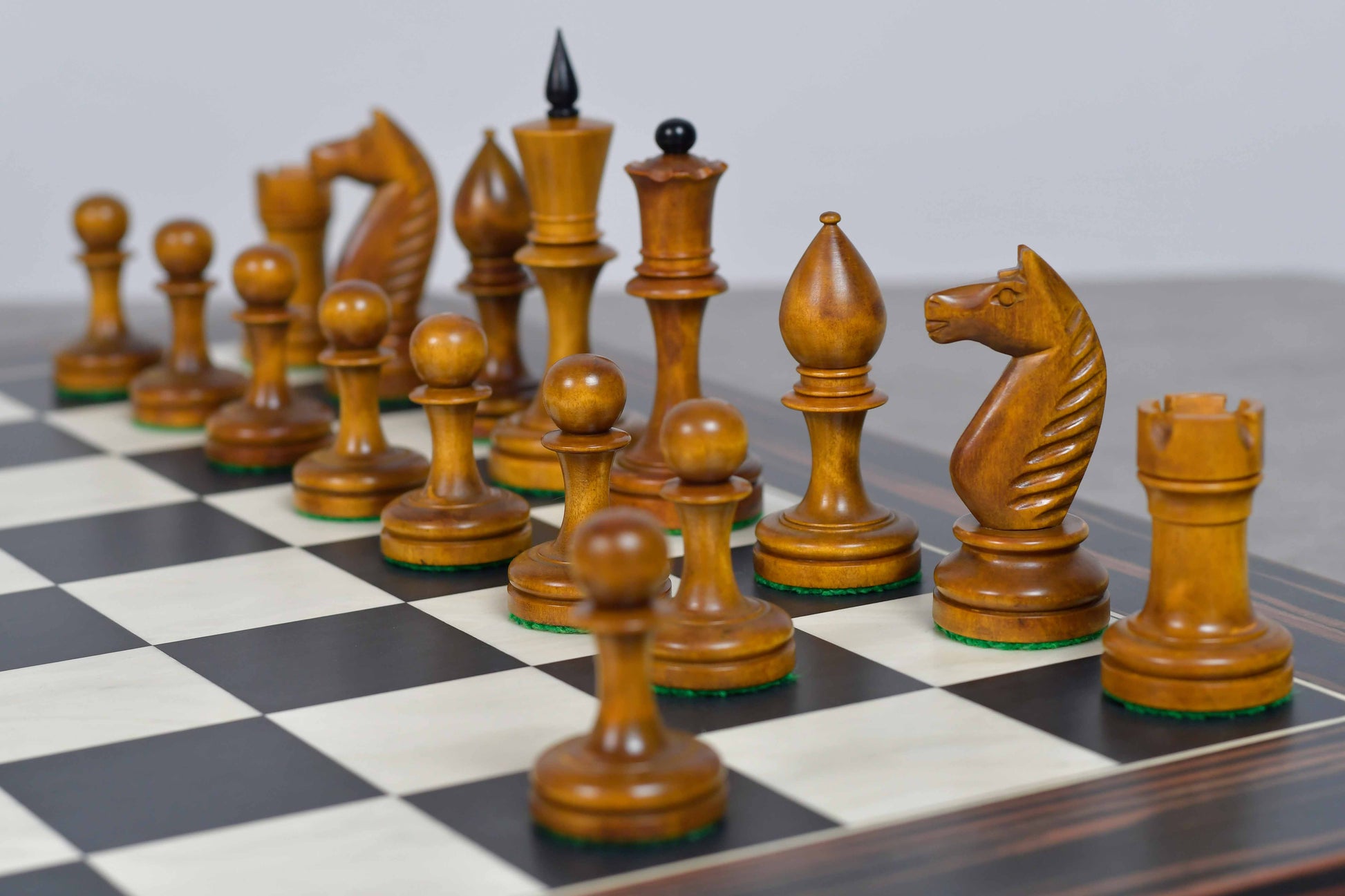 A set of wooden chess pieces arranged on a black-and-white checkered chessboard against a neutral gray background.